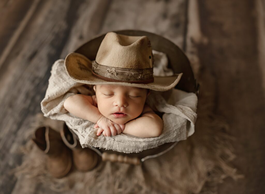 baby boy in cowboy hat and boots sleeping in a bucket during newborn photos 