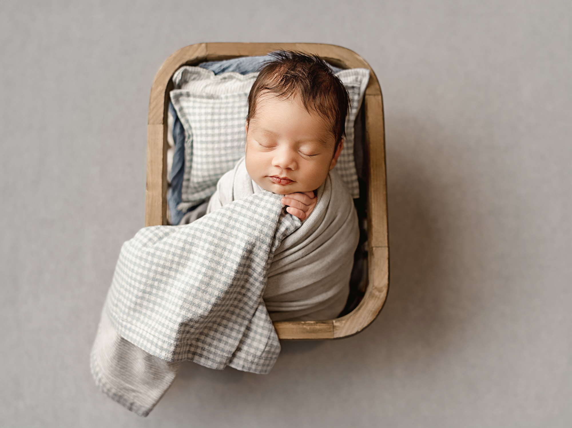 baby boy in light blue in a basket with a cute pillow sleeping during newborn session near sacramento