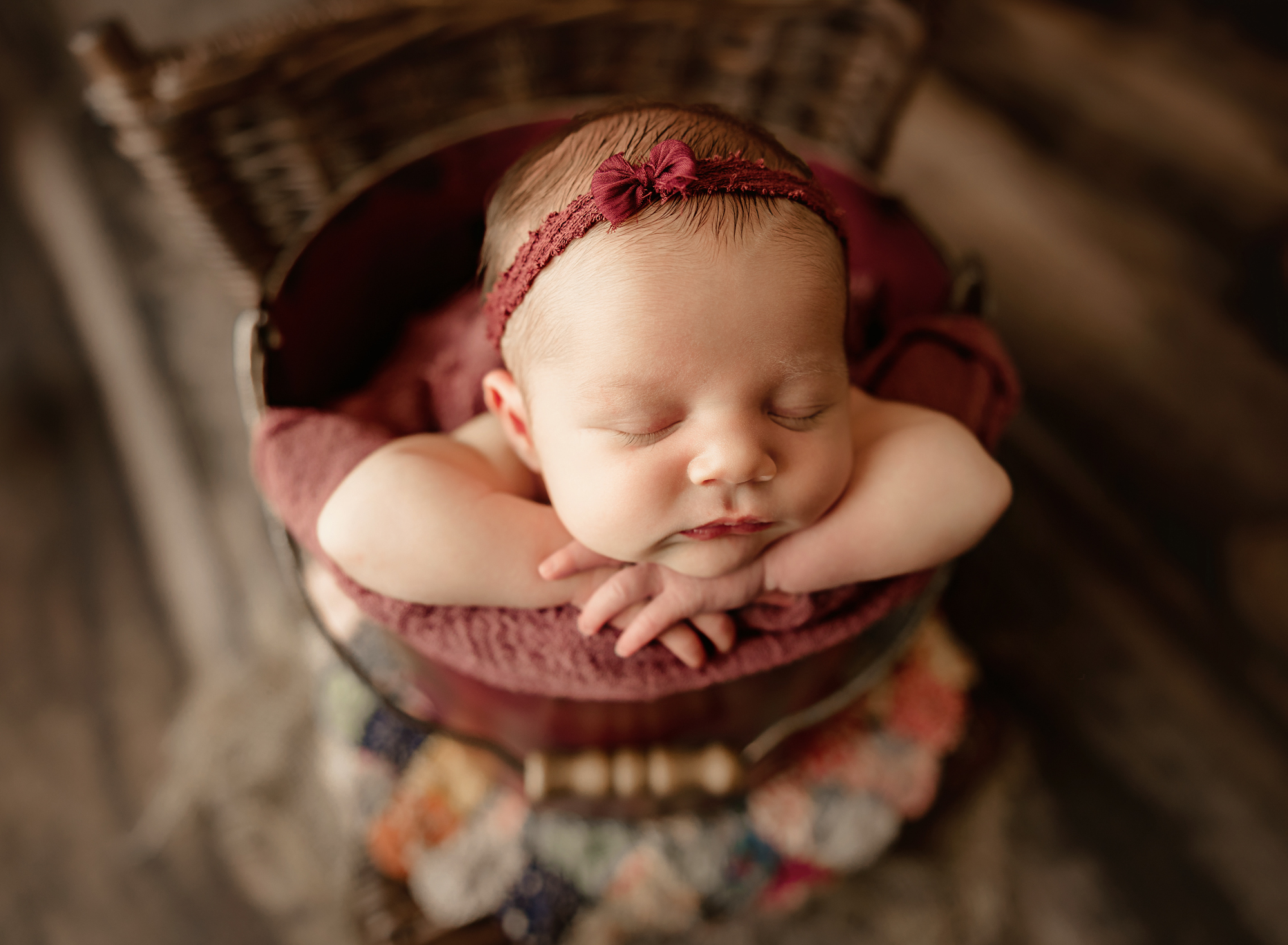 baby sleeping in a bucket sitting on a wicker chair with a quilted layer underneath during newborn photo session