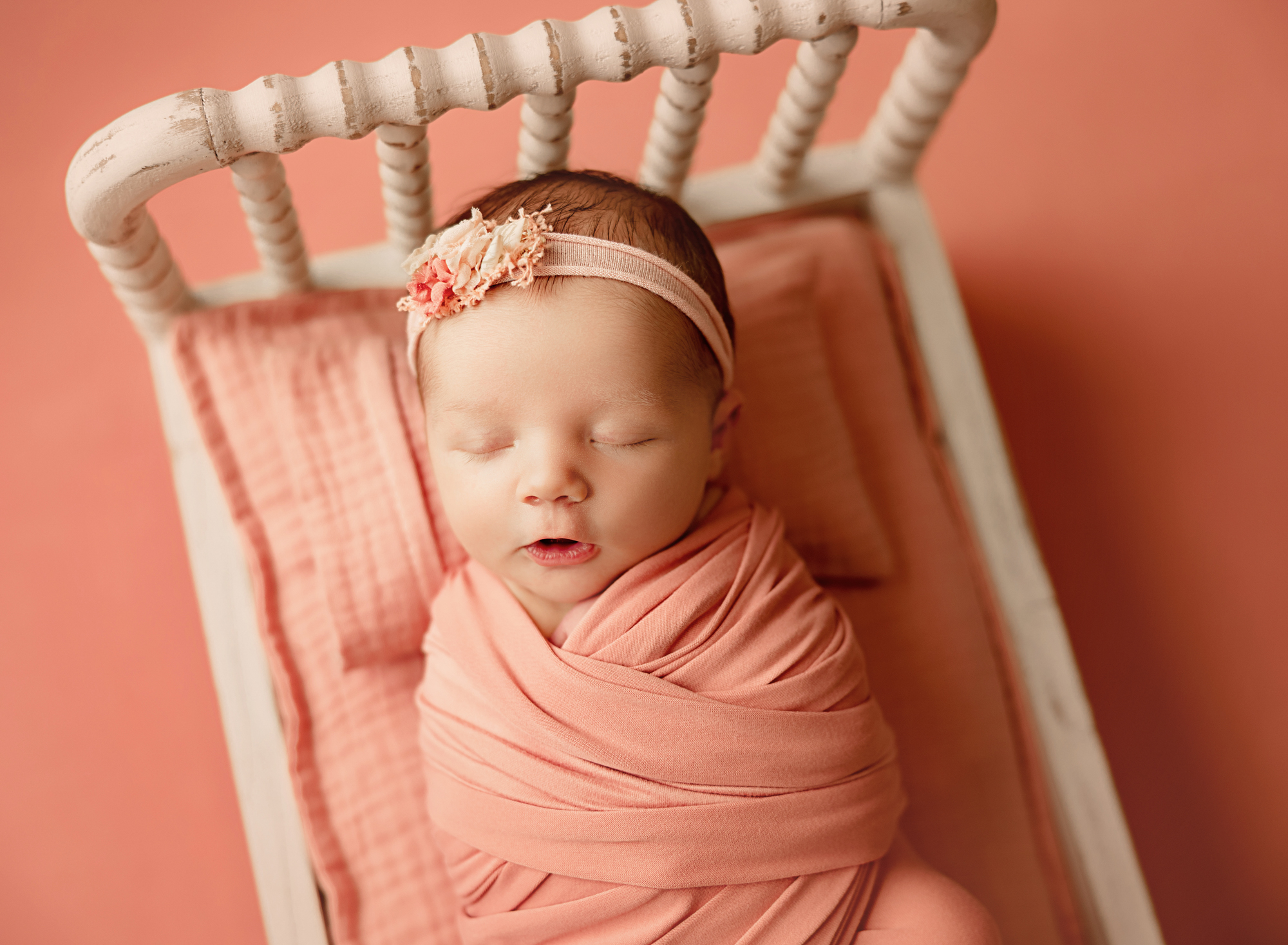 baby girl in pink tones sleeping in a cream colored bed during newborn session