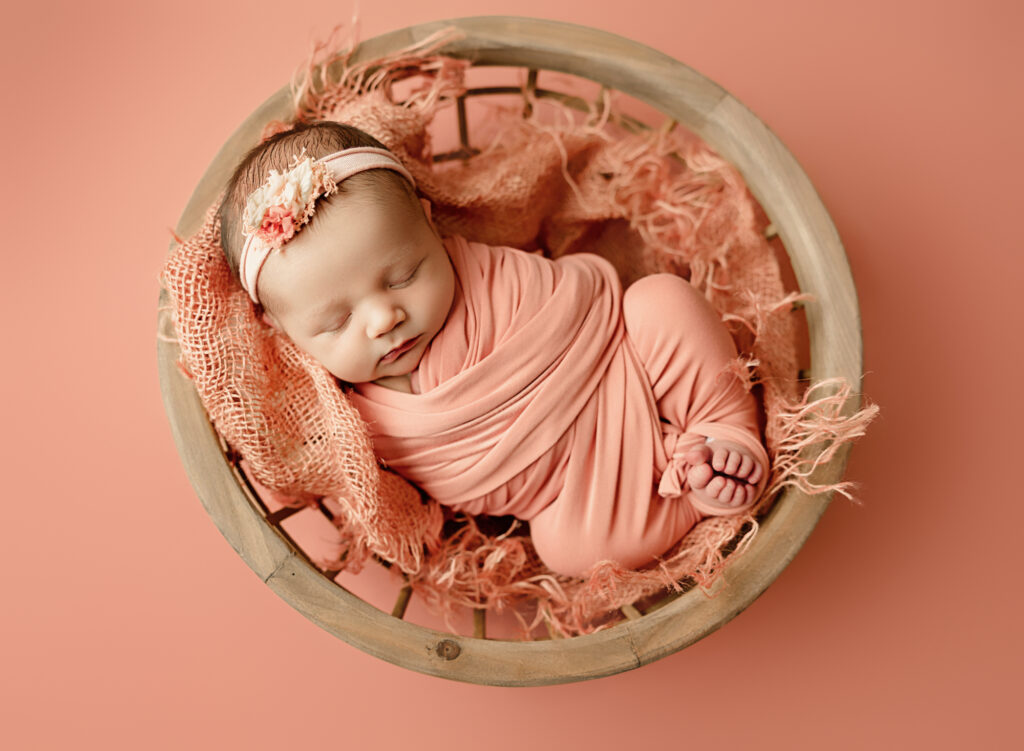 Baby wrapped in a pink wrap sleeping in a bowl for newborn photo session